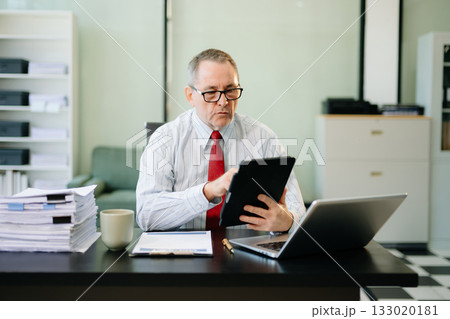 Mature businessman working in office with laptop, tablet, and notes. Perfect for business, finance, accounting 133020181
