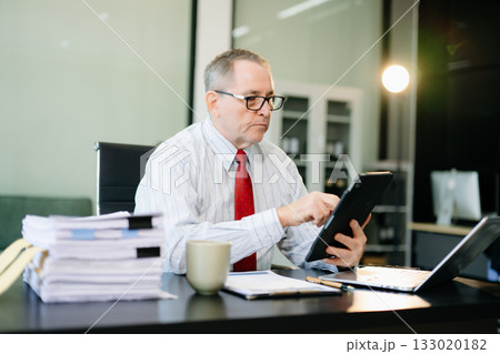 Mature businessman working in office with laptop, tablet, and notes. Perfect for business, finance, accounting Mature businessman working in office with laptop, tablet, and notes. Perfect for business, finance, accounting 133020182