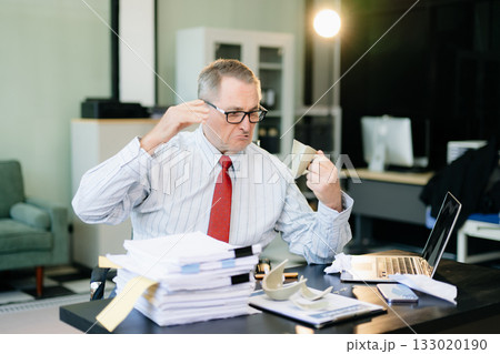 Angry and irritated Mature Businessman sitting in the office of laptop with his keyboard tired from work. Overwork, stress Angry and irritated Mature Businessman sitting in the office of laptop with his keyboard tired from work. Overwork, stress 133020190