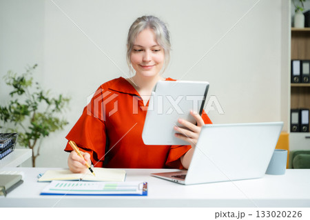young woman compares documents while working at her laptop in a modern office. Concept of paperwork, analysis, productivity 133020226