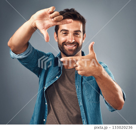 Frame, face and portrait of man in studio on gray background with happiness, confident and smile. Finger border, fashion and happy male person with hand sign for picture, photography and perspective 133020236