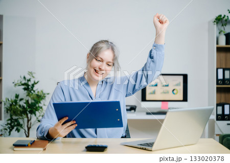 businesswoman celebrating success while analyzing reports in a modern office. Ideal for finance, accounting, achievement, statistics, and business growth themes. businesswoman celebrating success while analyzing reports in a modern office. Ideal for finance, accounting, achievement, statistics, and business growth themes. 133020378