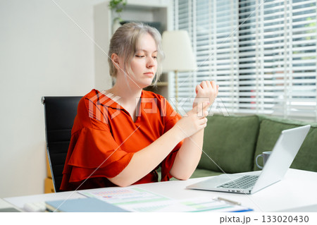 Young woman touching her neck in pain while working on laptop in bright office. Concept of workplace discomfort, poor posture, stress, and remote job fatigue. Young woman touching her neck in pain while working on laptop in bright office. Concept of workplace discomfort, poor posture, stress, and remote job fatigue. 133020430