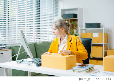 Young female entrepreneur running an SME, packing products, managing online store, shipping orders, and working from home. Perfect for ecommerce, delivery, and business themes. Young female entrepreneur running an SME, packing products, managing online store, shipping orders, and working from home. Perfect for ecommerce, delivery, and business themes. 133020513