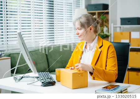 Young female entrepreneur running an SME, packing products, managing online store, shipping orders, and working from home. Perfect for ecommerce, delivery, and business themes. Young female entrepreneur running an SME, packing products, managing online store, shipping orders, and working from home. Perfect for ecommerce, delivery, and business themes. 133020515