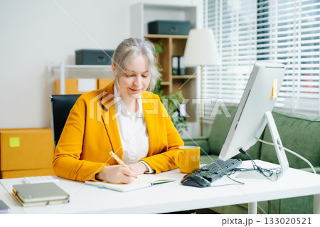 Young SME businesswoman in yellow blazer celebrates successful ecommerce delivery, smiling with parcel in hand at office desk. Online retail win. Real people. 133020521