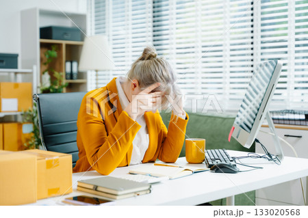 Young female SME worker in yellow blazer feeling tired and stressed while working at office desk. Facing burnout, deadline pressure, and mental fatigue. 133020568