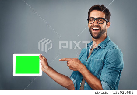 Happy man, tablet and pointing on mockup green screen for advertising against a grey studio background. Portrait of male person with smile showing technology display, chromakey or copy space branding 133020693