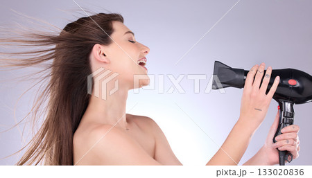 Beauty, straight hair and a woman blowing her hairstyle in studio on a gray background for grooming or style. Salon, cosmetics or salon with an attractive young female indoor to blowdry while styling Beauty, straight hair and a woman blowing her hairstyle in studio on a gray background for grooming or style. Salon, cosmetics or salon with an attractive young female indoor to blowdry while styling 133020836