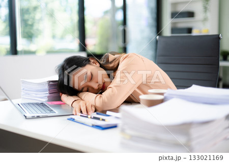 verworked Asian woman falls asleep on desk with paperwork, laptop, and coffee. Office fatigue, deadline stress, and burnout concept verworked Asian woman falls asleep on desk with paperwork, laptop, and coffee. Office fatigue, deadline stress, and burnout concept 133021169