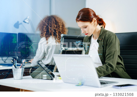 Two female fintech developers collaborating on finance apps, data analytics, and UI UX design in a high tech startup office 133021508