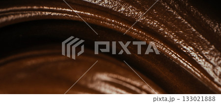 Macro close-up of melted dark chocolate with glossy texture and smooth swirls, abstract background of creamy liquid chocolate for dessert design and confectionery concept 133021888