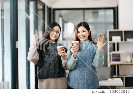 Happy two Asian business woman holding coffee cup in coworking office 133022019