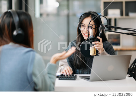 Young woman and Asian woman wearing headphones and doing a live podcast for their channel, communication for radio podcast and technology concept 133022090