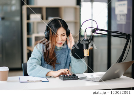 Young smiling woman wearing headphones and talking into a microphone at the radio station, entertainment a live podcast for their channel 133022091