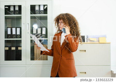 Focused businesswoman working on laptop while holding tablet at desk with documents and coffee. Concept of productivity, multitasking 133022229