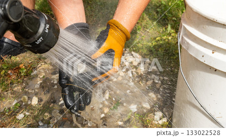 Hands of a worker using a pressure washer to clean gravel and stones, showcasing the effectiveness of outdoor cleaning techniques and tools 133022528