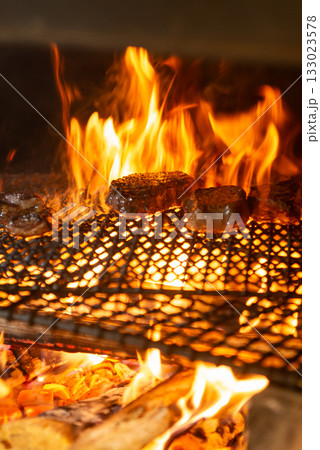 薪火で焼き上げる肉料理　炎が立ち上る炭火グリルの臨場感 133023578