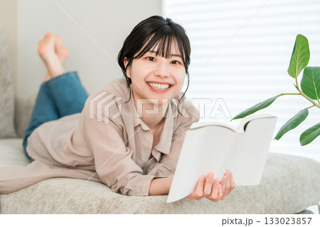 リビングのソファーで読書する若いアジア人女性 リビングのソファーで読書する若いアジア人女性 133023857