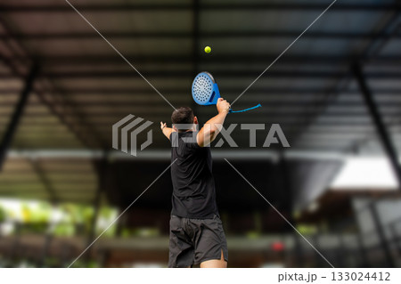 Male player serving a yellow padel ball indoors at a sleek court 133024412