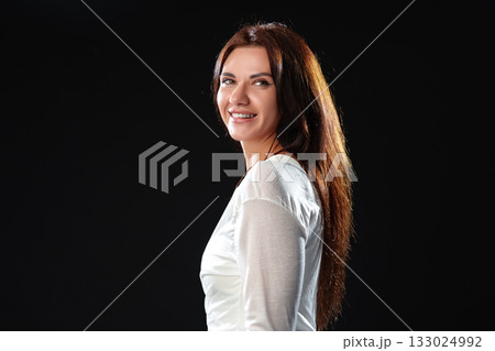Smiling woman in a white shirt poses confidently against a dark background 133024992
