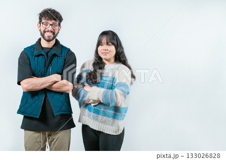 Smiling young couple with crossed arms looking at camera, isolated. Cheerful young multiethnic couple with arms crossed, isolated 133026828