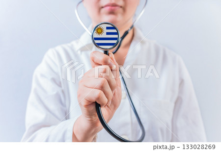 Female doctor holding stethoscope with Uruguay flag. National health system of Uruguay Female doctor holding stethoscope with Uruguay flag. National health system of Uruguay 133028269