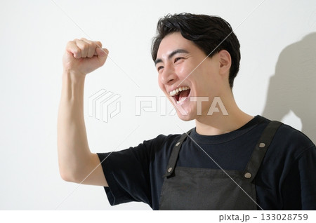 ガッツポーズをするエプロンをつけた男性 133028759