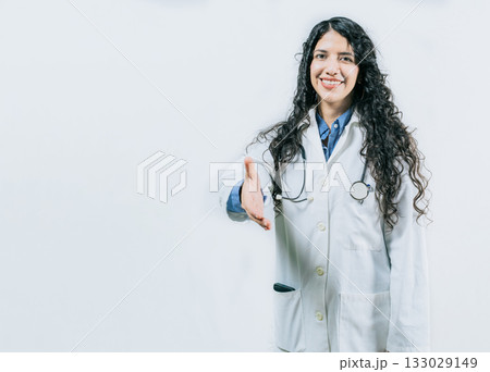 Smiling female doctor gesturing welcome, isolated. Latin female doctor shaking hands at the camera gesturing welcome 133029149