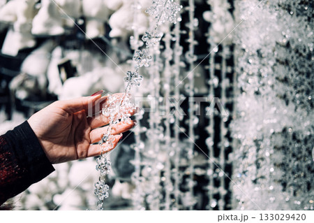 Hand holding a delicate Christmas garland of faceted snowflake-shaped beads in a sparkling holiday retail display. Crystal bead garlands, faceted design, luxury accents, gem-inspired decoration 133029420