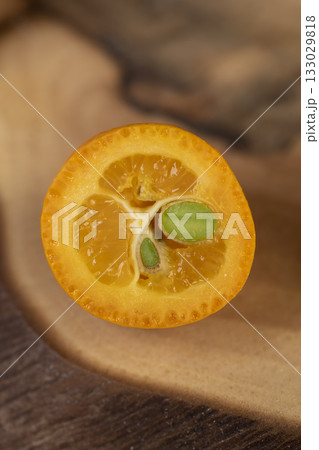 cut ripe kumquat cut in half on a wooden table, a group of scattered and sliced kumquat fruits on a wooden table and board 133029818