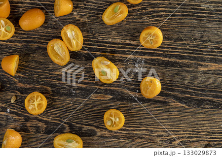 lots of ripe orange kumquat cut in half on a wooden table, a group of scattered kumquat fruits on a wooden table and board 133029873