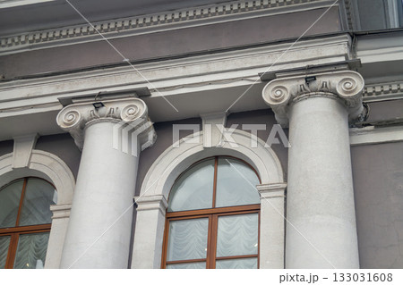 Facade fragment of an old classicism style building with Ionic columns and an arched window. Architectural background symbolizing justice, government, education, or culture and finance. 133031608