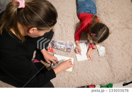 Mother and daughter enjoy creative time together at home drawing on the carpet, fostering imagination and bonding through art. Mother and daughter enjoy creative time together at home drawing on the carpet, fostering imagination and bonding through art. 133033076