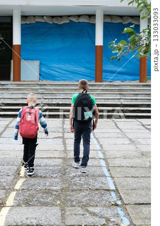Two young boys with backpacks are walking towards a building, likely heading to school on a paved path with colored lines marking the way. Two young boys with backpacks are walking towards a building, likely heading to school on a paved path with colored lines marking the way. 133033093