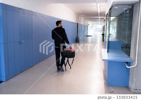 Male adult walking in sports center hallway with backpack and sports bag 133033415
