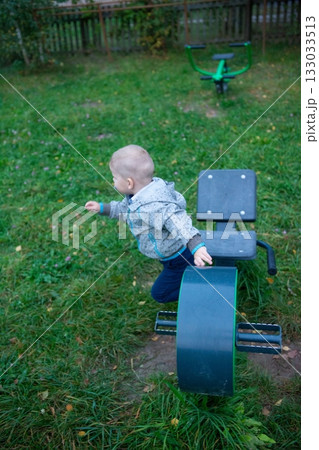 Child explores outdoor fitness equipment, engaging in playful activities within a grassy park setting on a cloudy day, promoting active lifestyles. 133033513