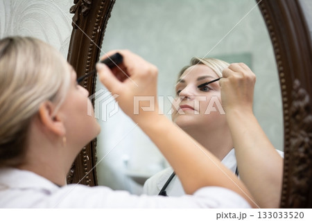 Woman applying makeup in mirror, enhancing beauty routine. Personal care and reflection are key for self-care and confidence boosting. 133033520