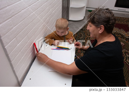 Grandmother and toddler bonding over art, creating colorful drawings. Intergenerational learning and playful interaction in cozy home setting. Grandmother and toddler bonding over art, creating colorful drawings. Intergenerational learning and playful interaction in cozy home setting. 133033847