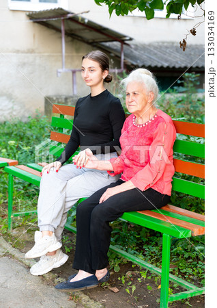 Two generations connect on a bench in the park as the warm afternoon sun casts a gentle glow on their smiles and shared moments of affection and warmth 133034169
