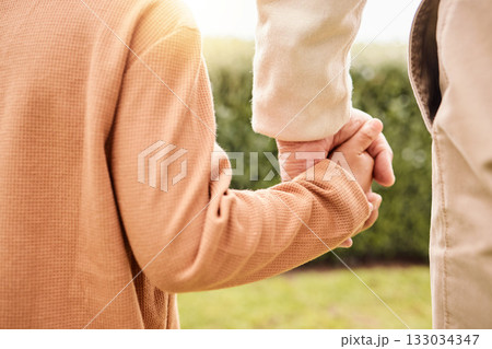 Kid, park and holding hands with parents on vacation, adventure walk or freedom in nature together. Young child child, outdoor happiness or holiday for helping hand, support and walking in sunshine 133034347