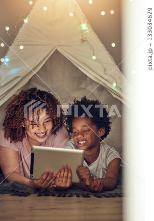 Tablet, black family and mother with kid in tent at night watching movie, video and having fun in home. Technology, love and smile of happy mixed race mom bonding with boy child while streaming film. 133034629