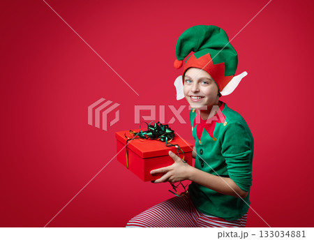 Merry Christmas concept. Smiling funny boy in Santa's elf costume holding 133034881