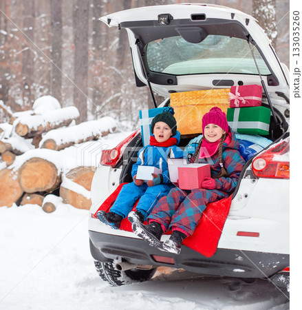 Merry Christmas. Happy New Year. Happy family children sitting in car loaded with boxes of gifts and Christmas tree against the background Merry Christmas. Happy New Year. Happy family children sitting in car loaded with boxes of gifts and Christmas tree against the background 133035260