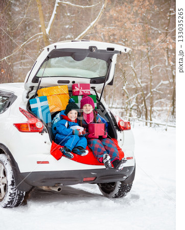 Merry Christmas. Happy New Year. Happy family children sitting in car loaded with boxes of gifts and Christmas tree against the background Merry Christmas. Happy New Year. Happy family children sitting in car loaded with boxes of gifts and Christmas tree against the background 133035265