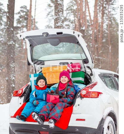 Merry Christmas. Happy New Year. Happy family children sitting in car loaded with boxes of gifts and Christmas tree against the background of forest Merry Christmas. Happy New Year. Happy family children sitting in car loaded with boxes of gifts and Christmas tree against the background of forest 133035295