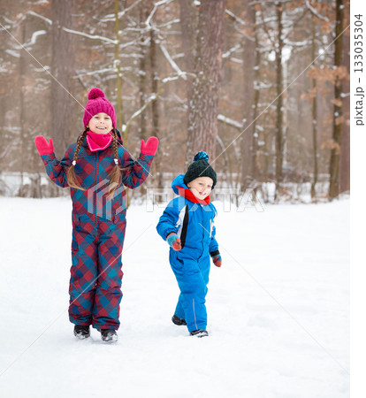 Children and their mom play together in fresh snow, dressed in warm colorful winter clothes, surrounded by trees in winter wonderland. Children and their mom play together in fresh snow, dressed in warm colorful winter clothes, surrounded by trees in winter wonderland. 133035304