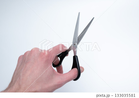 Hand Holding Scissors with Black Handles on Light Background Hand Holding Scissors with Black Handles on Light Background 133035581