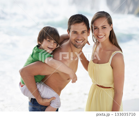 Family, child and happy portrait at beach on travel holiday in summer with a smile and piggy back fun. A man, woman and kid or son playing together on vacation at sea with love, care and happiness 133035710