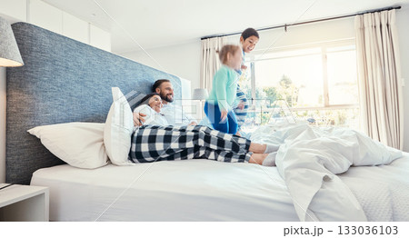 Love, family and playing in bedroom, quality time and happiness in the morning, vacation and cheerful. Mother, father and children on bed, jumping and joyful with smile, bonding and loving together 133036103